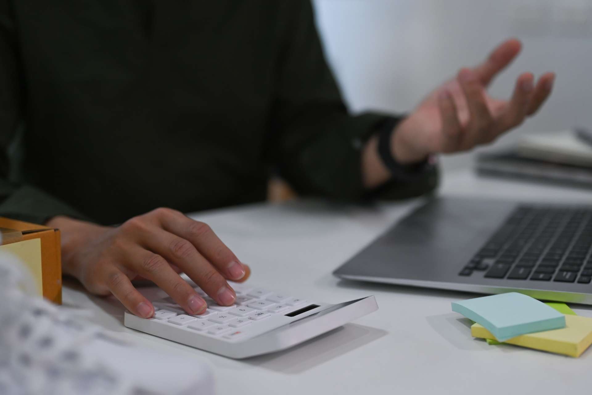 Pessoa em frente ao notebook, realizando c&aacute;lculos em uma calculadora.