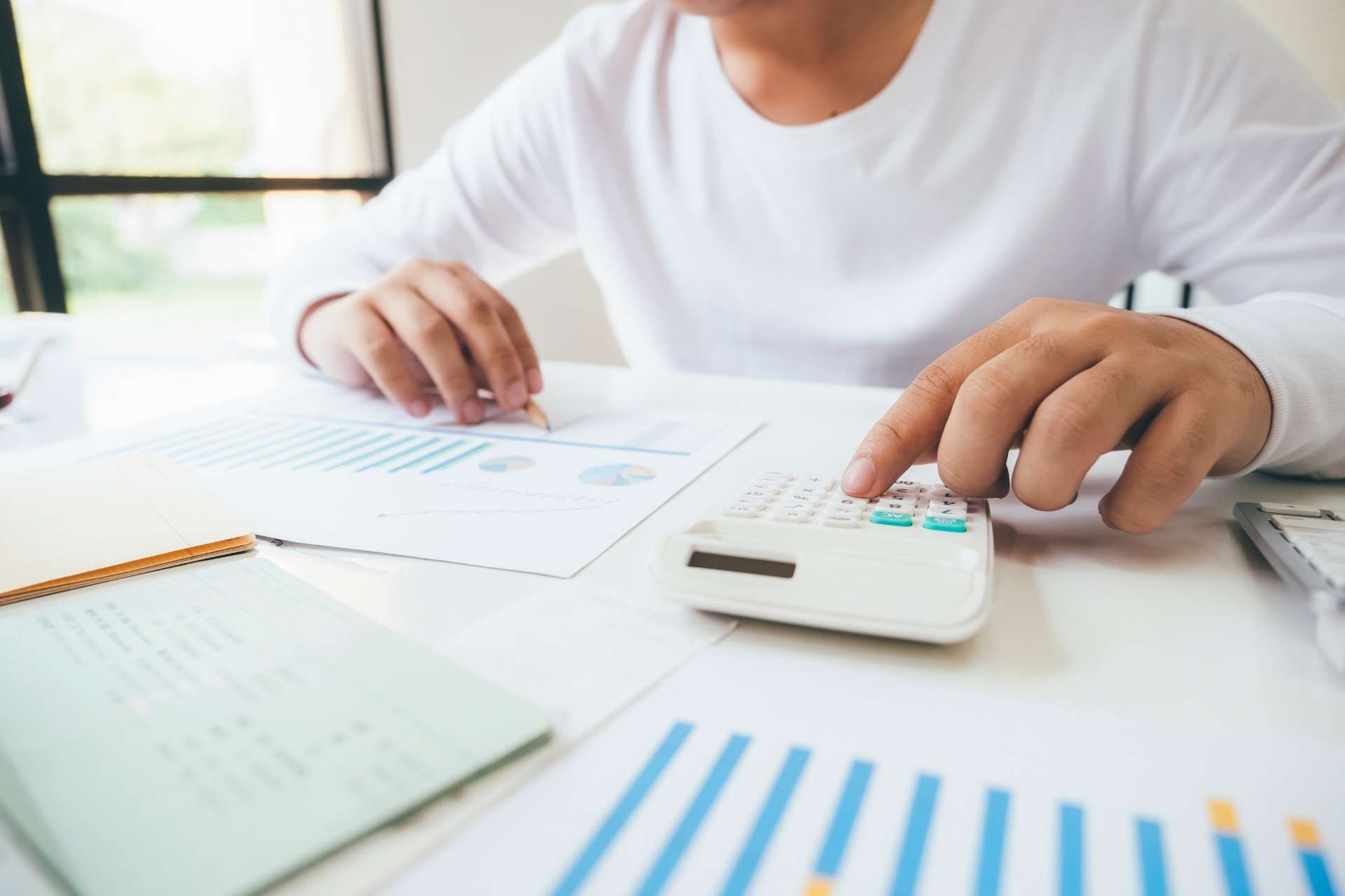 Pessoa analisando dados e gr&aacute;ficos e realizando contas em calculadora.