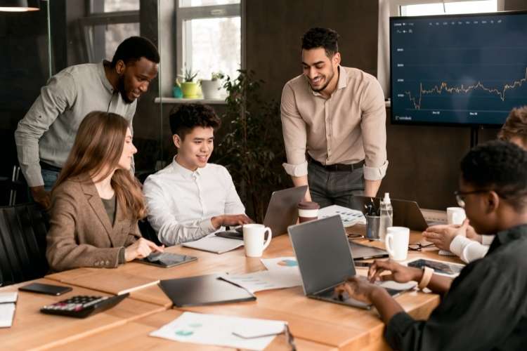 Equipe de trabalho composta de homens e mulheres, ao computador, sorrindo enquanto trabalham.