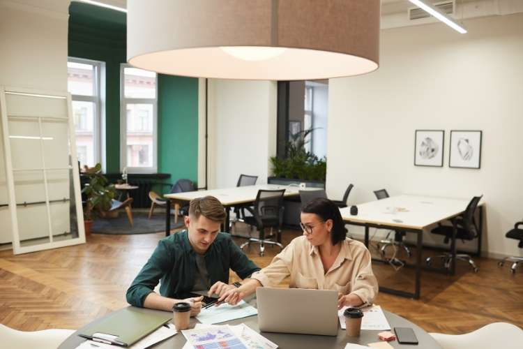 Homem e mulher com papéis e notebook sobre a mesa, conversando sobre o que estão vendo.